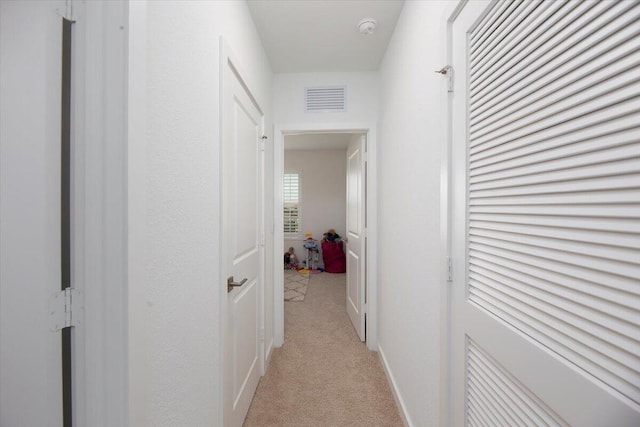 hall featuring baseboards, visible vents, and light carpet