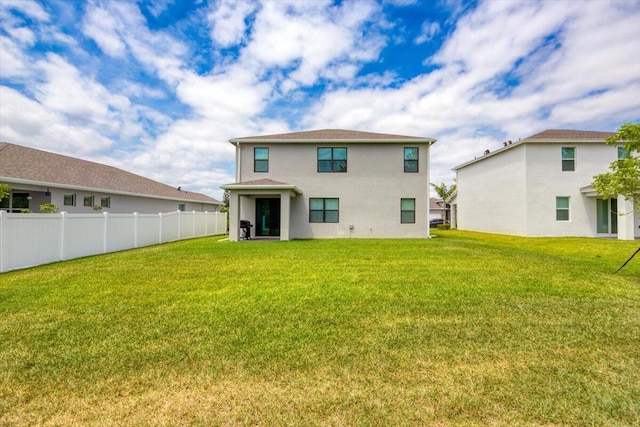 back of house with stucco siding, a lawn, and fence