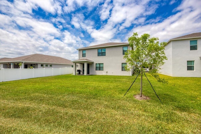 rear view of property with stucco siding, fence, and a yard