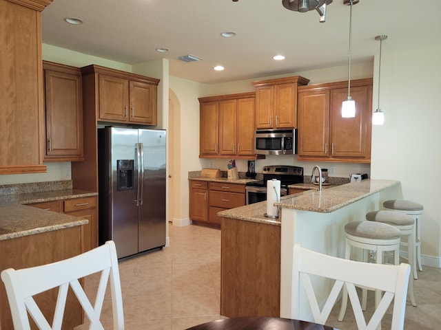 kitchen with visible vents, light stone countertops, brown cabinets, baseboards, and stainless steel appliances