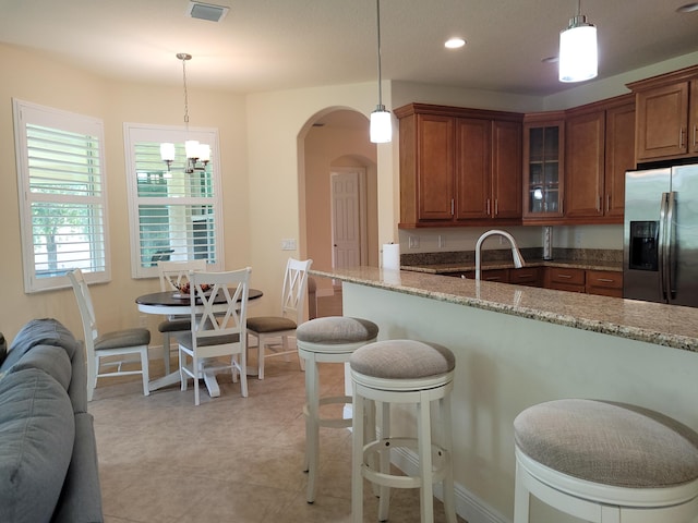kitchen featuring stainless steel refrigerator with ice dispenser, brown cabinetry, visible vents, and glass insert cabinets