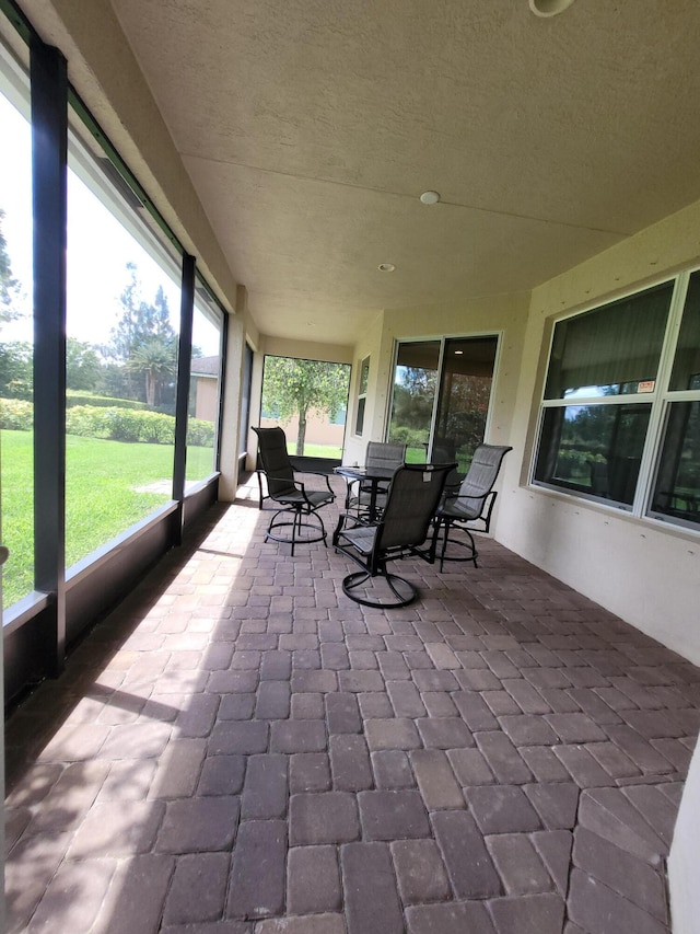 sunroom / solarium with outdoor dining area, a textured ceiling, and brick floor