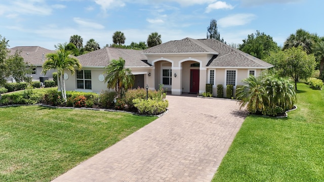 single story home with decorative driveway, a shingled roof, a front lawn, and stucco siding