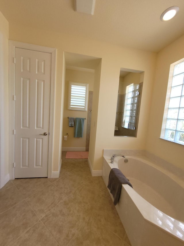 full bath featuring a healthy amount of sunlight, baseboards, tile patterned flooring, and a garden tub