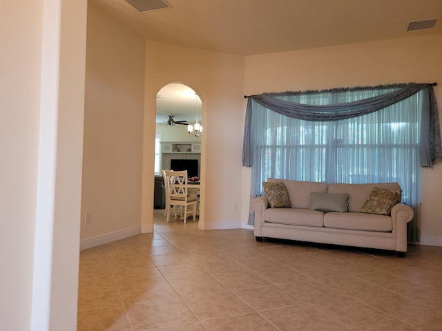 living room featuring a ceiling fan, visible vents, arched walkways, tile patterned floors, and baseboards