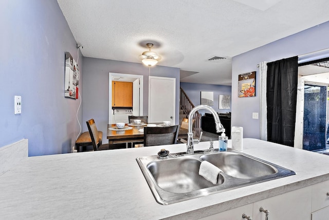 kitchen with a textured ceiling, visible vents, a sink, light countertops, and white cabinets
