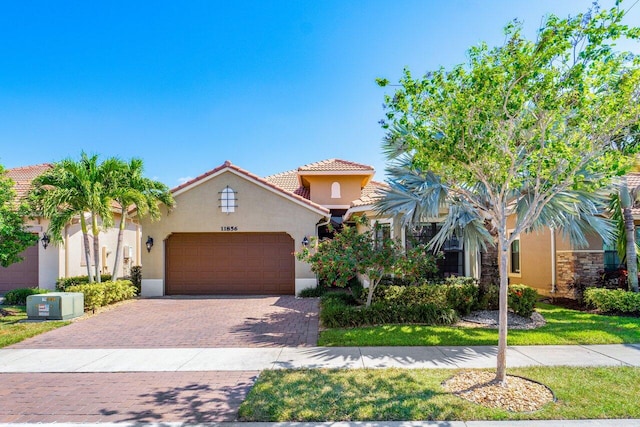 mediterranean / spanish house with decorative driveway, an attached garage, a tile roof, and stucco siding