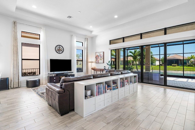 living area featuring a raised ceiling, light wood finished floors, recessed lighting, and a towering ceiling