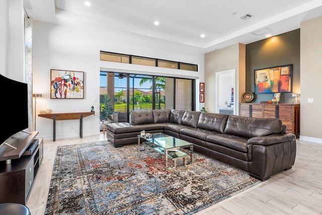 living room with a towering ceiling, wood finished floors, baseboards, recessed lighting, and a tray ceiling
