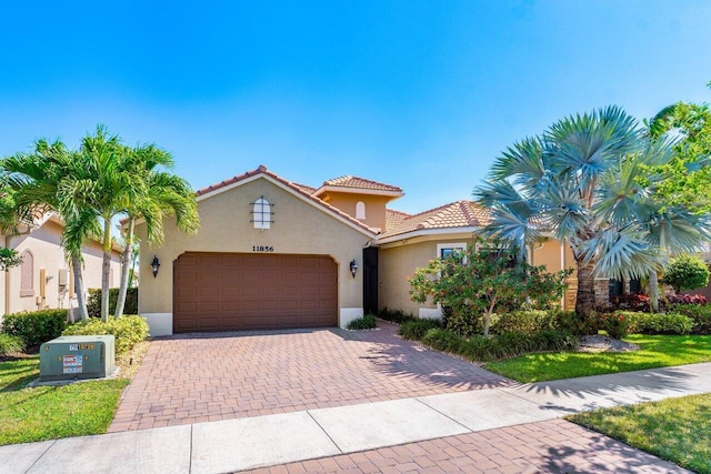 mediterranean / spanish-style home featuring a tiled roof, decorative driveway, a garage, and stucco siding
