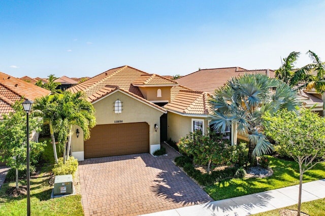 mediterranean / spanish home featuring decorative driveway, a garage, stucco siding, and a tile roof