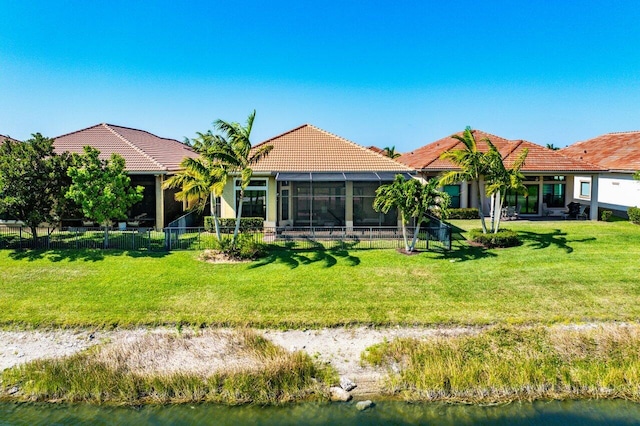 back of property with a water view, fence, a yard, and a tile roof