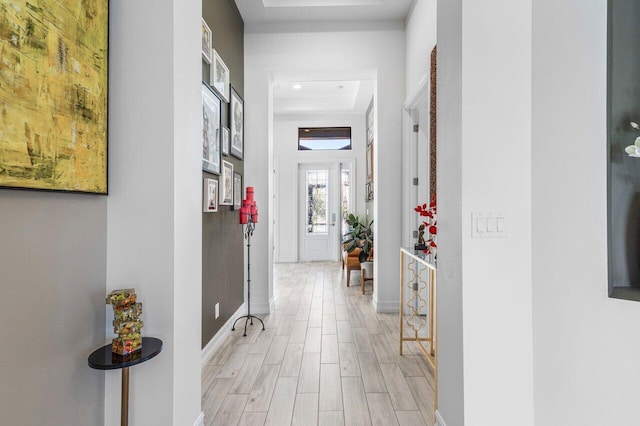 hall featuring recessed lighting, a tray ceiling, baseboards, and light wood-type flooring