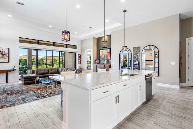 kitchen featuring light stone counters, a sink, dishwasher, open floor plan, and baseboards