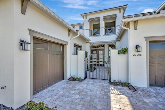 property entrance featuring fence, an attached garage, stucco siding, a gate, and a balcony