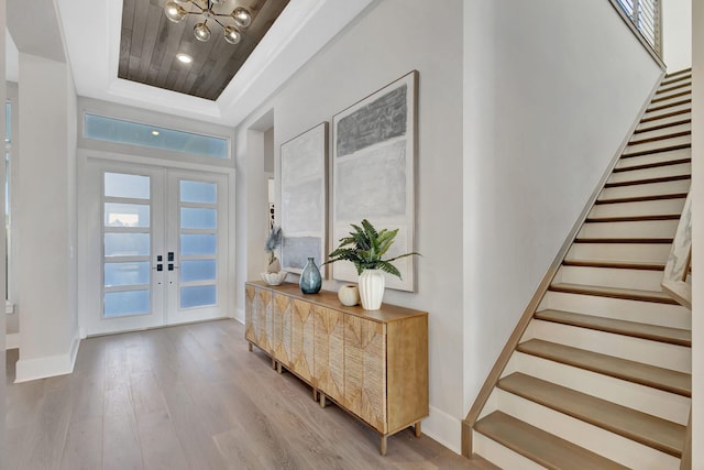 entrance foyer with wood finished floors, baseboards, stairway, a raised ceiling, and french doors