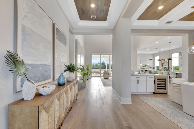 hallway with a raised ceiling, plenty of natural light, light wood finished floors, and beverage cooler