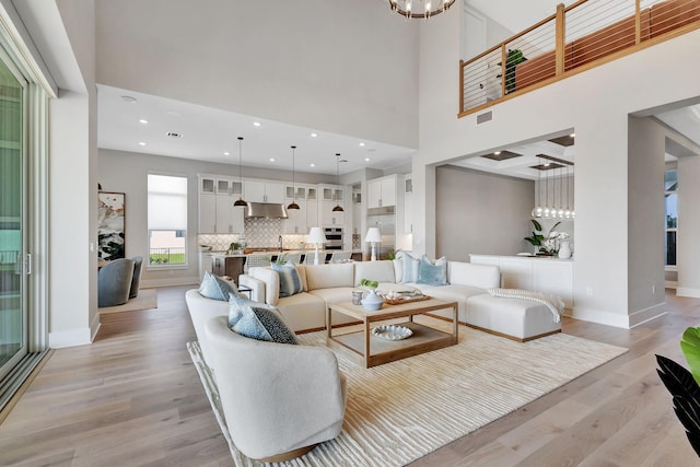living area with visible vents, an inviting chandelier, a towering ceiling, baseboards, and light wood-style flooring