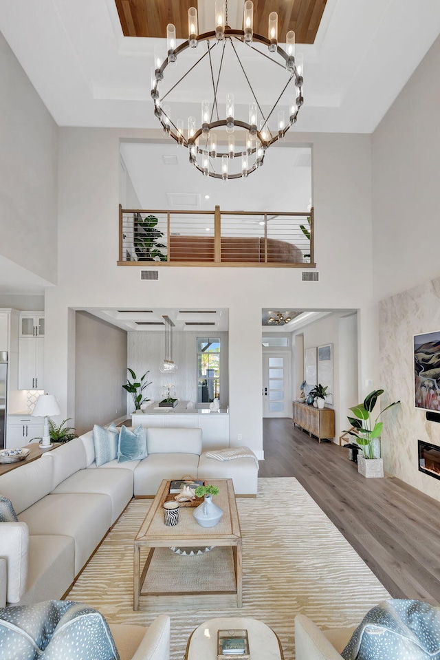 living room featuring a high ceiling, a chandelier, wood finished floors, and visible vents