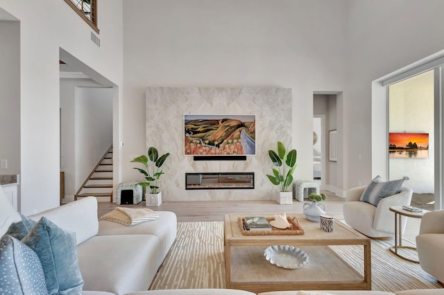 living room featuring a towering ceiling, stairs, wood finished floors, a high end fireplace, and visible vents