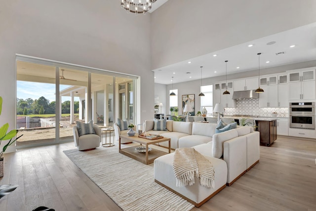 living area featuring a high ceiling, a chandelier, light wood-style flooring, recessed lighting, and visible vents