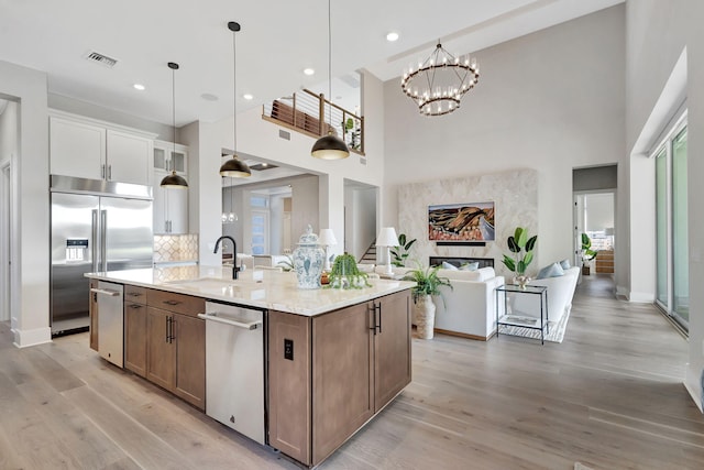 kitchen with a kitchen island with sink, a towering ceiling, visible vents, a sink, and stainless steel appliances