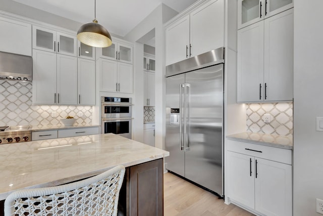 kitchen featuring white cabinets, light stone counters, light wood-style flooring, stainless steel appliances, and decorative backsplash