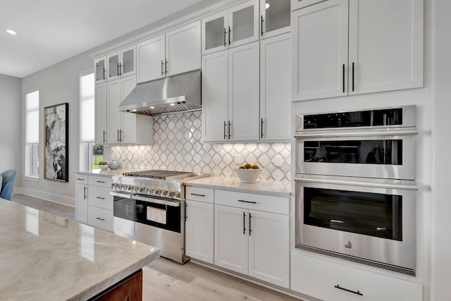kitchen with appliances with stainless steel finishes, tasteful backsplash, light wood-type flooring, white cabinets, and under cabinet range hood