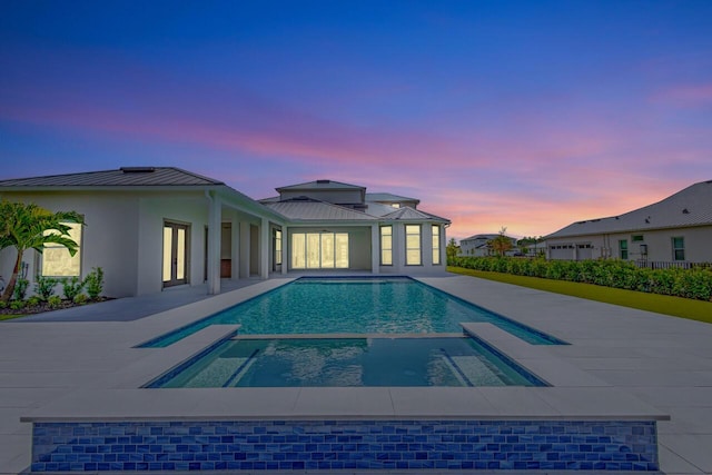 pool at dusk with a patio area and a pool with connected hot tub