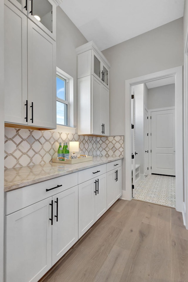 kitchen with light stone countertops, light wood-style flooring, white cabinetry, decorative backsplash, and glass insert cabinets