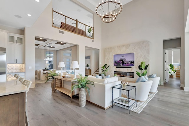 living area featuring a towering ceiling, a chandelier, a high end fireplace, and light wood-style floors