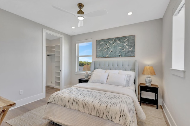 bedroom featuring a walk in closet, light wood finished floors, recessed lighting, baseboards, and a closet