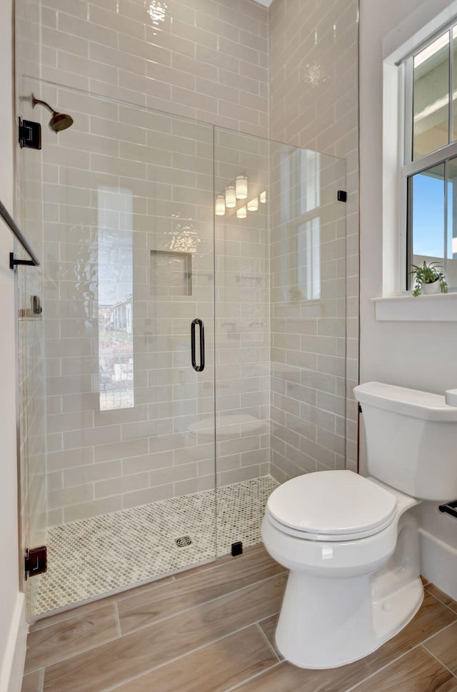 full bath with toilet, wood finish floors, and a stall shower