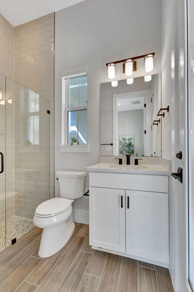bathroom featuring a stall shower, wood finish floors, vanity, baseboards, and toilet