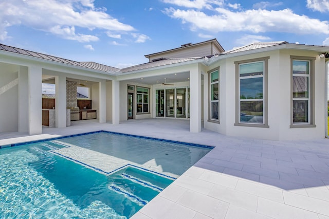 back of house featuring a patio, an outdoor pool, a standing seam roof, an outdoor kitchen, and metal roof