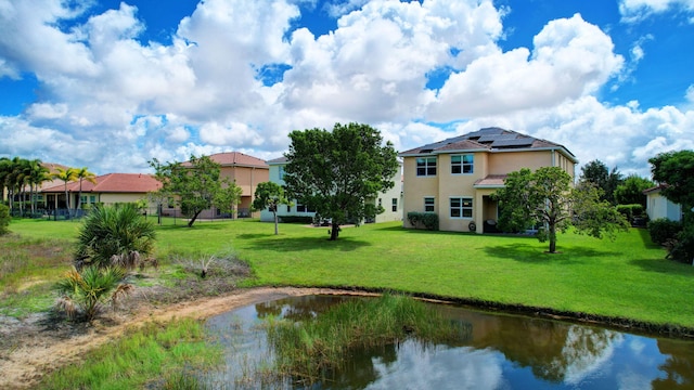 exterior space with a lawn, a water view, roof mounted solar panels, and stucco siding