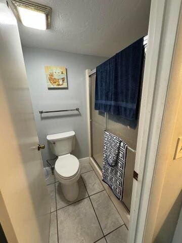 full bath featuring tile patterned floors, a textured ceiling, a stall shower, and toilet