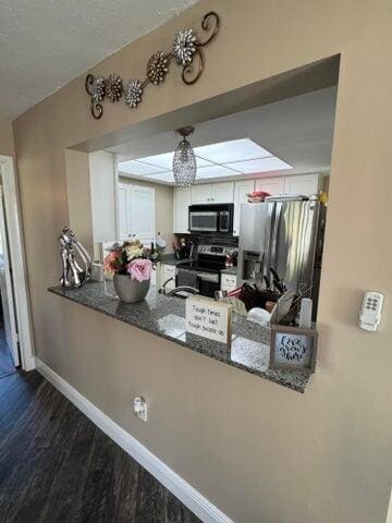 kitchen with a peninsula, baseboards, dark wood-style floors, dark stone counters, and stainless steel appliances