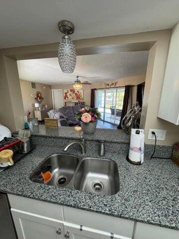 kitchen with a sink, dark stone counters, a ceiling fan, and white cabinets