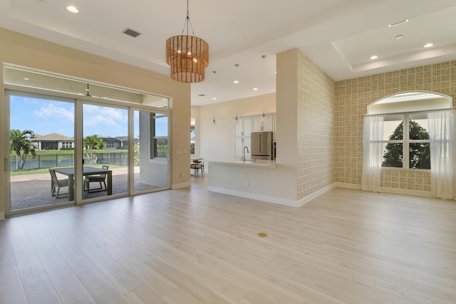 9252 SW Miracoli Way, Port Saint Lucie, FL 34987 - unfurnished living room featuring a sink, light wood-type flooring, an inviting chandelier, a water view, and baseboards