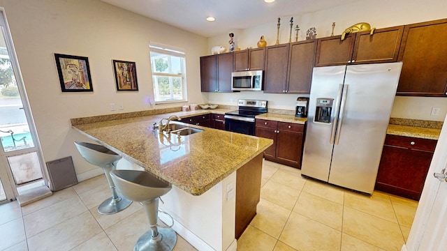 2323 NW Padova St, Port Saint Lucie, FL 34986 - kitchen with a peninsula, a breakfast bar, light stone counters, a sink, and stainless steel appliances