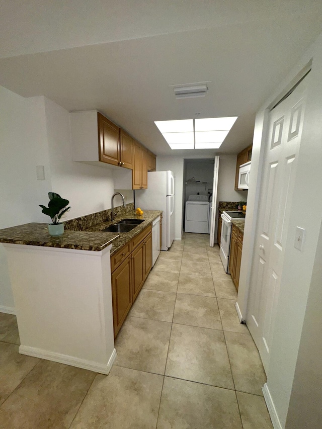 kitchen with brown cabinets, a sink, white appliances, washer / clothes dryer, and dark stone counters