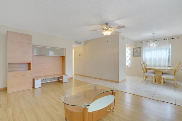 living area with light wood finished floors, a chandelier, a ceiling fan, a textured ceiling, and baseboards
