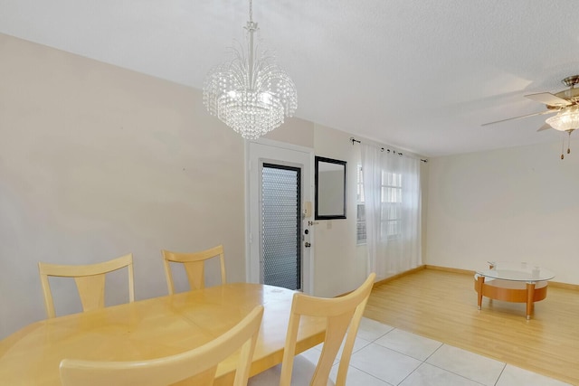 dining room featuring light tile patterned flooring, a ceiling fan, a chandelier, baseboards, and a textured ceiling