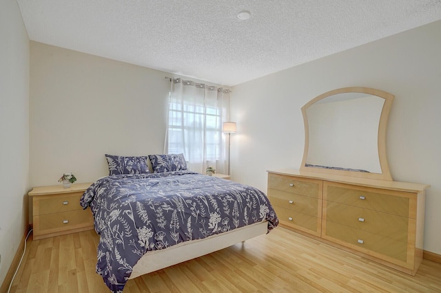 bedroom featuring light wood-style flooring, a textured ceiling, and baseboards