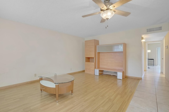 living room with a ceiling fan, light wood-style flooring, baseboards, and a textured ceiling