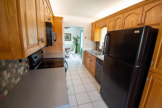 kitchen with brown cabinetry, light tile patterned floors, a sink, backsplash, and black appliances