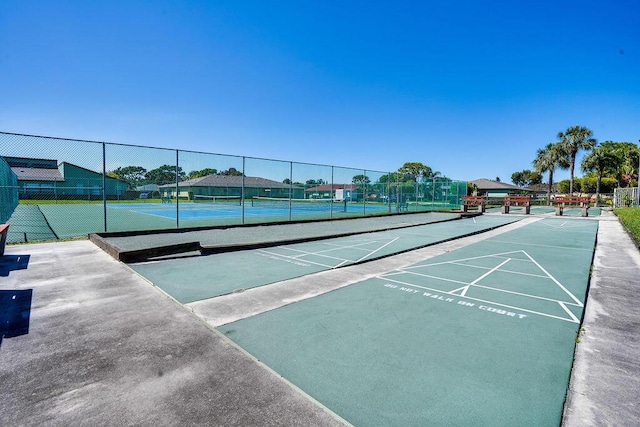 view of property's community featuring fence, shuffleboard, and a tennis court