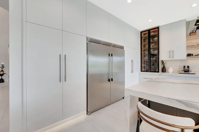 kitchen with open shelves, glass insert cabinets, white cabinets, built in fridge, and light tile patterned floors