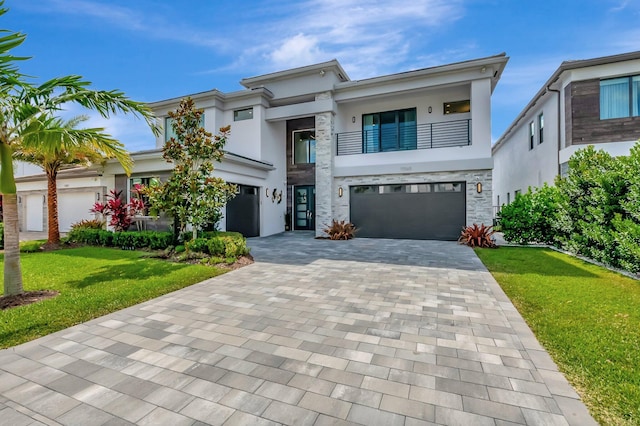 view of front of house with an attached garage, a front lawn, stucco siding, decorative driveway, and a balcony